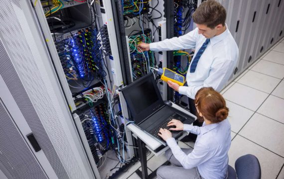 Team of technicians using digital cable analyser on servers in large data center